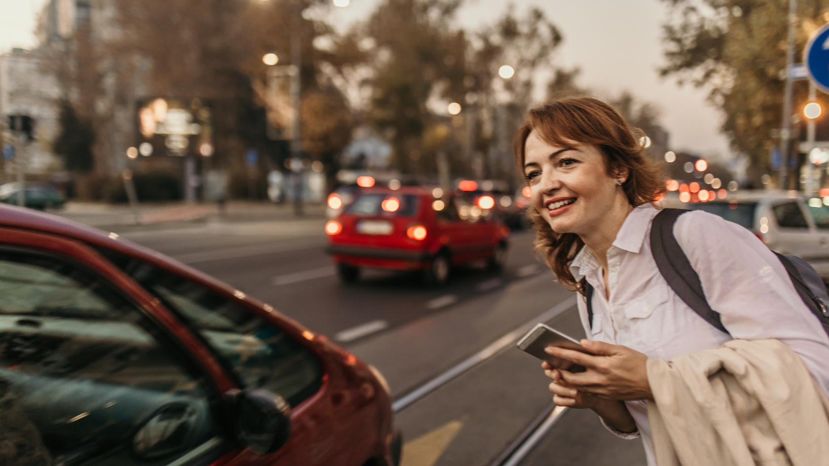 A woman walking down a street next to a red car